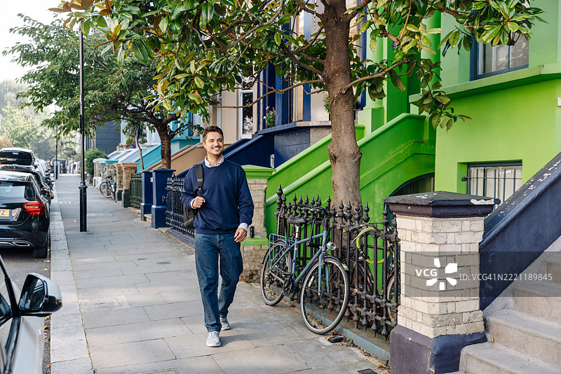 快乐微笑的男子在伦敦诺丁山色彩缤纷的街道上漫步图片素材