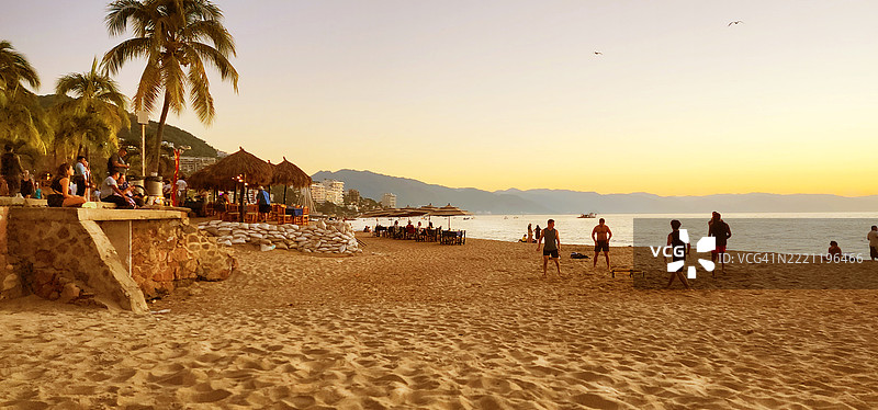 普埃尔托瓦亚尔塔海滩的橙色日落场景，人们在享受时光。图片素材