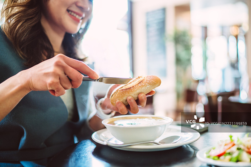 微笑的女性在温馨的咖啡馆用餐时涂抹黄油在面包上图片素材