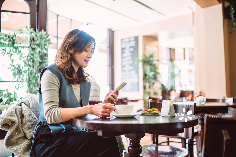 愉快的女性在舒适的咖啡馆享受咖啡并查看手机图片素材