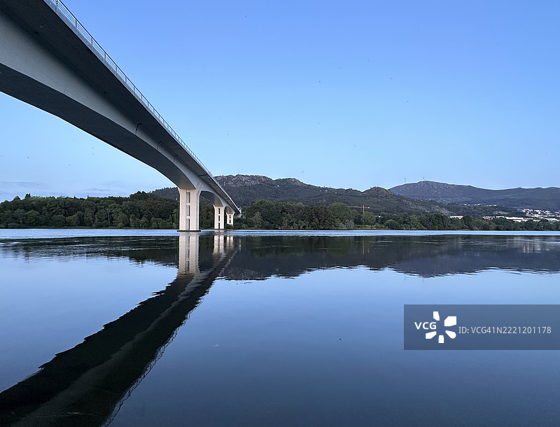 友谊桥在黄昏时分映照在宁静的米尼奥河水面上，托米奥， Galicia图片素材