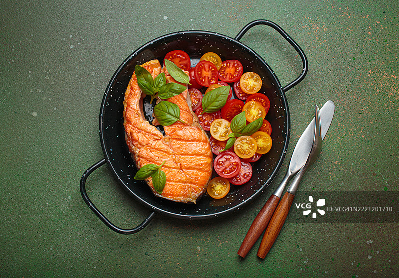 黑色盘子里的烤三文鱼排配樱桃番茄和罗勒叶图片素材