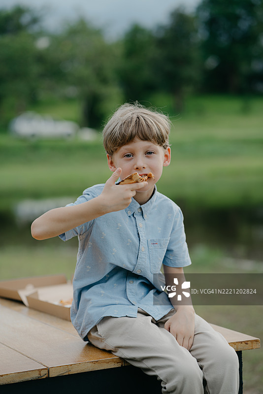 男孩坐在长椅上吃披萨图片素材