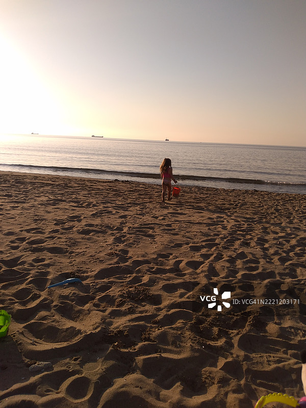 女孩背对海滩在日落时分的天空下站立图片素材