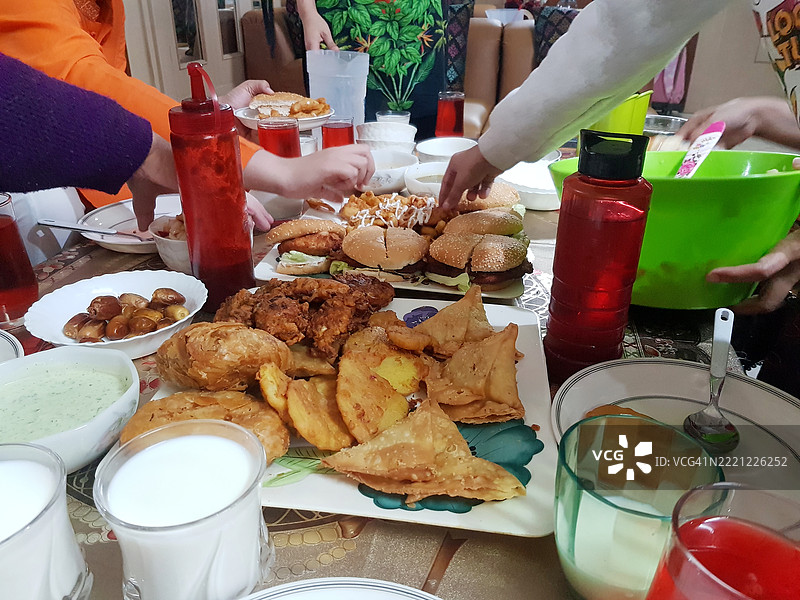 人手伸出抓取油炸萨莫萨、土豆饼或巴可拉，以及在家中斋月期间的牛奶。图片素材