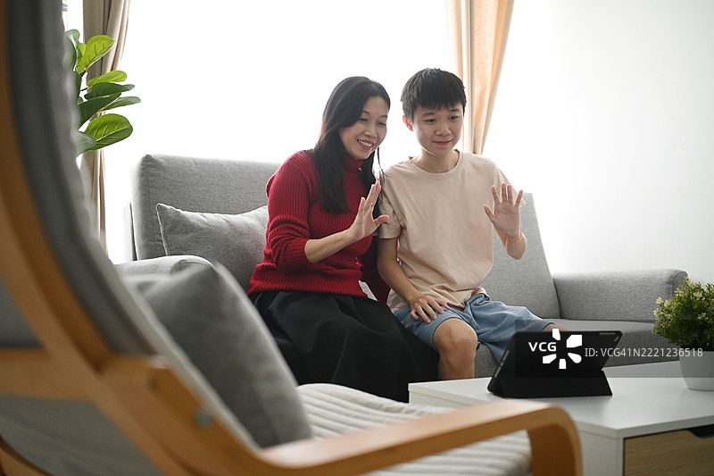 孩子和他的母亲在家里的沙发上通过手机视频聊天。图片素材