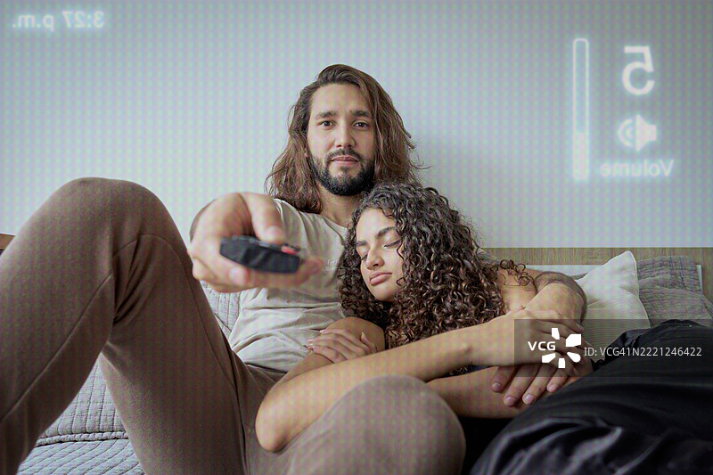 一个男人从电视的角度调低音量，以免吵醒他的伴侣。图片素材