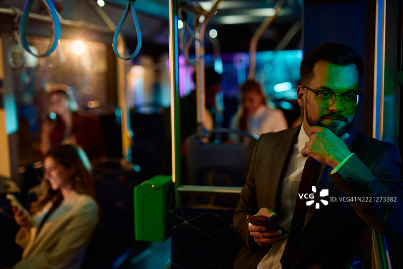 沉思的商人在夜间公交车上使用智能手机图片素材