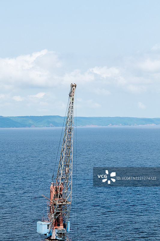 一座高大的港口起重机在铁路上，位于河边。一个用于卸货的巨大结构。图片素材