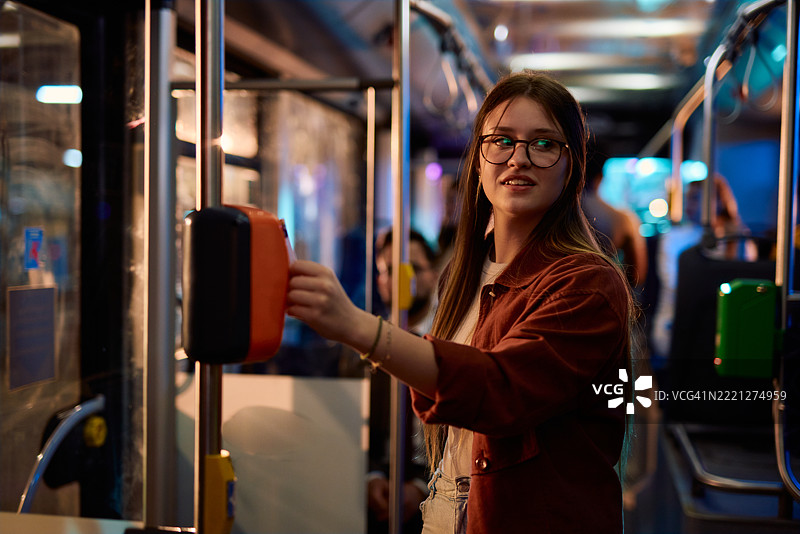 年轻女性在夜间公共交通上验证公交票图片素材