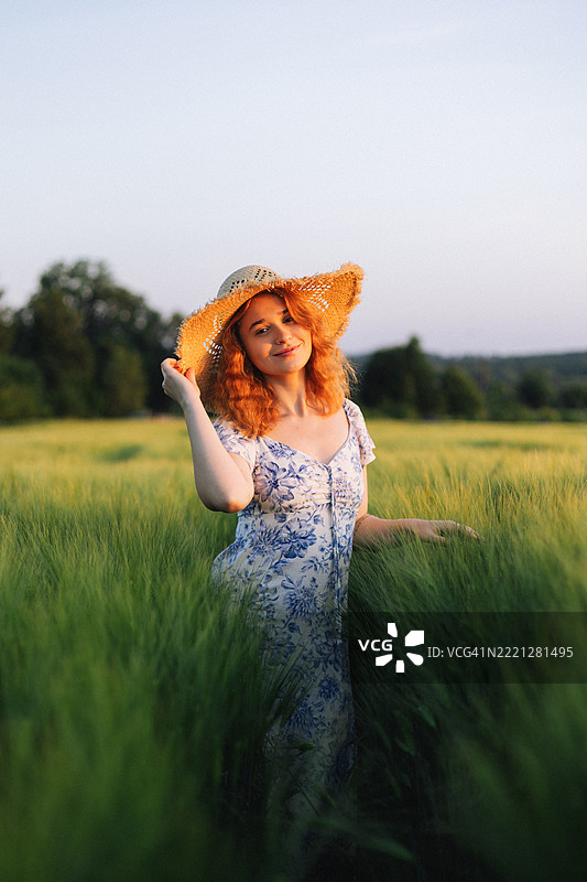 美丽的红发女子在郁郁葱葱的田野中戴着草帽的半身肖像图片素材