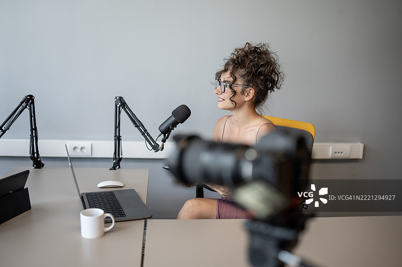 年轻女性在专业录音室中主持播客，手持麦克风图片素材