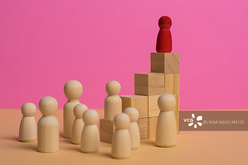 木制人偶注视着一个红色棋子攀登到不断增长的柱状图顶部，象征着成功。图片素材