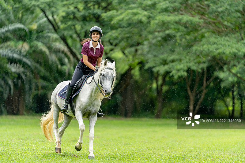 年轻的少女骑马在农场或公共花园的田野上奔跑，背景是一棵大树。图片素材