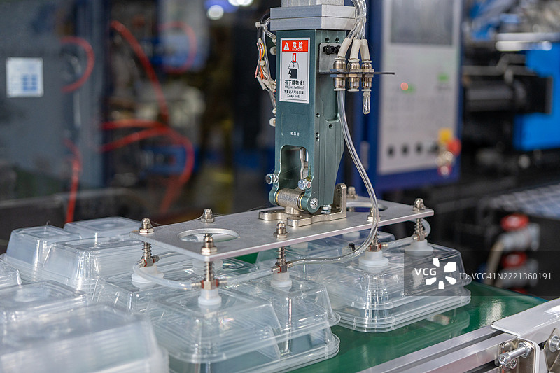 机器人手臂从注塑机进行物料搬运的过程。食品容器箱的生产过程由塑料注塑模具机完成。图片素材