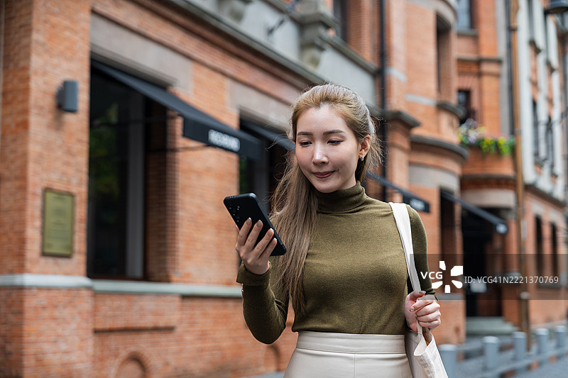 在上海外滩散步的亚洲女性游客，手持智能手机图片素材