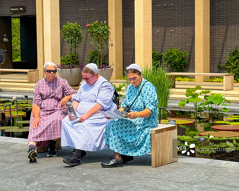 三位女性在宾夕法尼亚州肯尼特广场的朗伍德花园长椅上放松。图片素材
