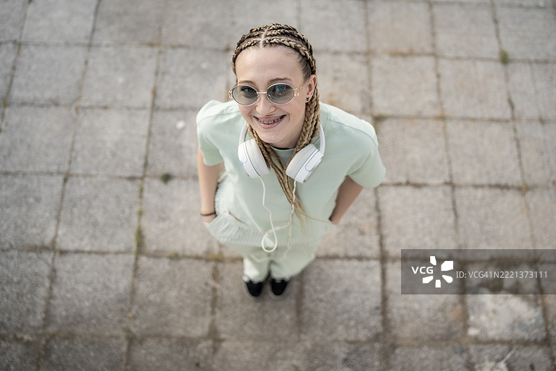 年轻女性在户外微笑，扎着辫子，戴着耳机图片素材