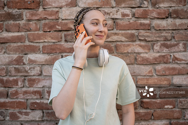在城市环境中，微笑的年轻女性戴着耳机打电话图片素材