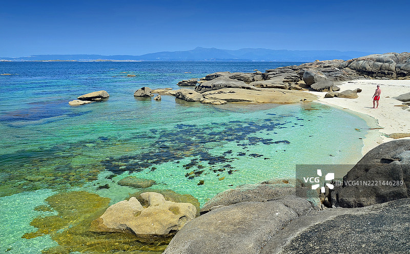 一位单身男子在西班牙加利西亚蓬特韦德拉的卡雷龙自然公园内，阿罗萨岛南部美丽的海湾享受阳光和海滩的一天。图片素材