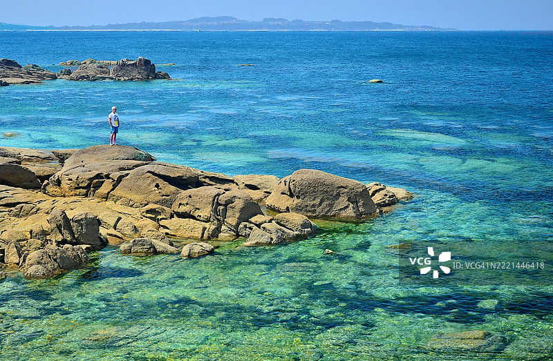 一位单身男子在西班牙加利西亚蓬特维德拉的卡雷龙自然公园内，阿罗萨岛南部美丽的海湾中享受阳光和海滩的一天。图片素材