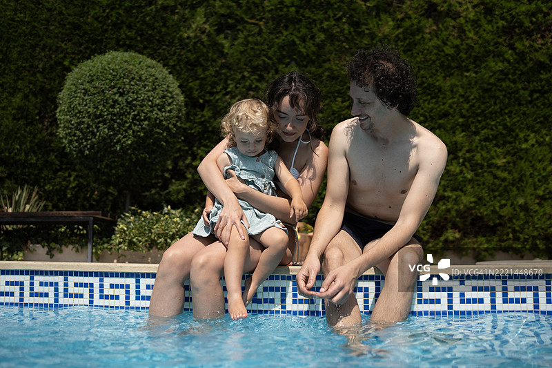 快乐的家庭在阳光明媚的日子里一起在明亮的游泳池旁放松图片素材