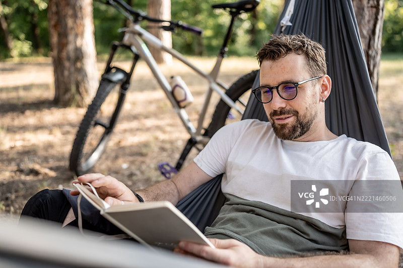 男人在户外的吊床上放松，阅读一本书图片素材