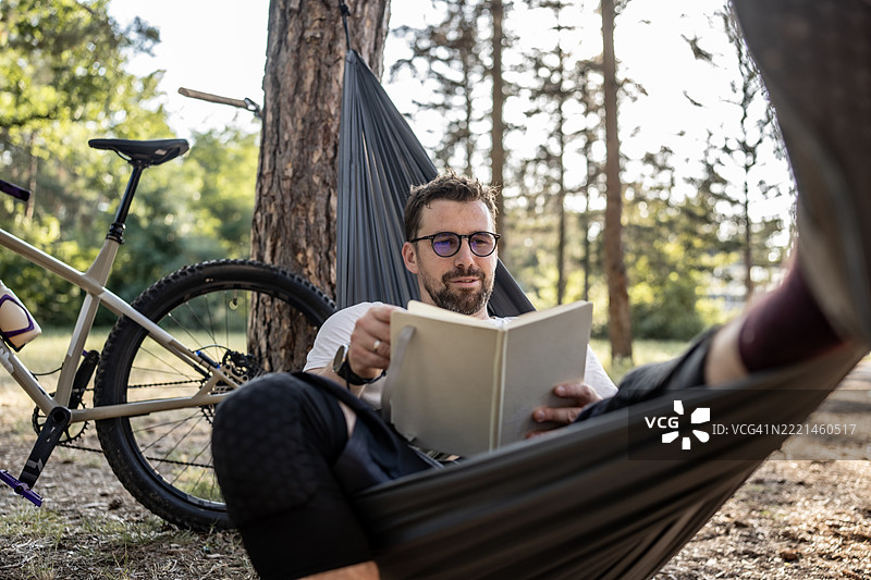 在大自然中，躺在吊床上阅读，旁边有一辆自行车，享受放松时光图片素材