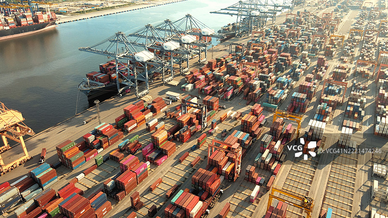 新加坡丹戎巴葛的货船停靠在码头，周围有装卸起重机和沿海工业港口，背景是城市风光和出口集装箱。图片素材
