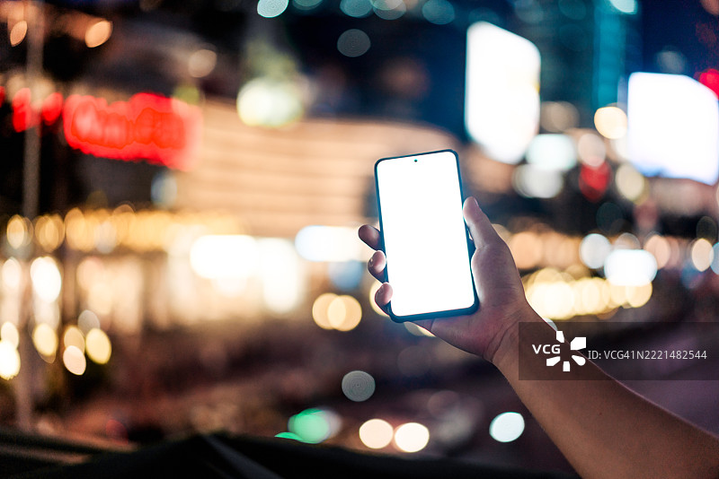 男性手部特写，手握智能手机，背景是灯光璀璨的现代城市街道夜景虚化效果。日常生活中的科技。生活方式与科技。图片素材