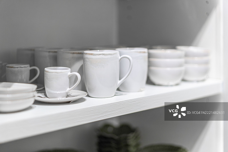 白色陶瓷杯整齐地排列在架子上。图片素材