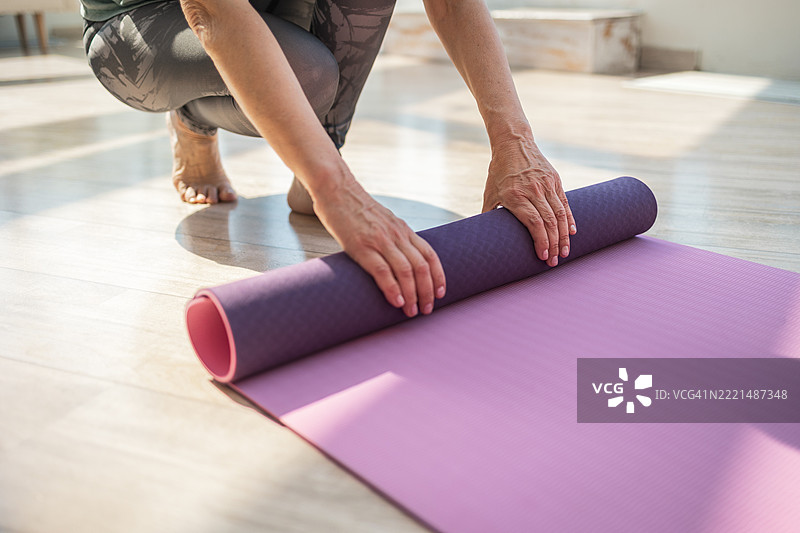 阳光明媚的现代房间里，一个人正在卷起粉色瑜伽垫的特写镜头图片素材