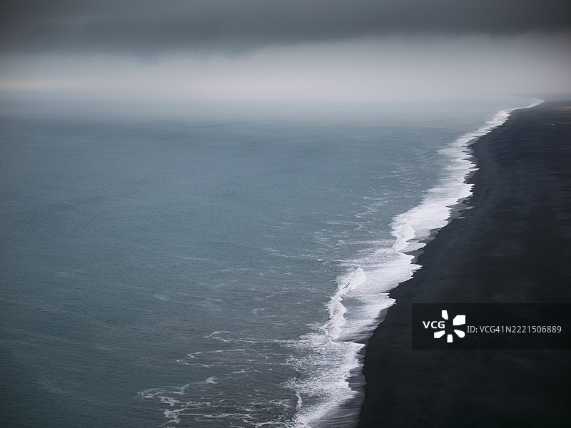 在雨天，白色的波浪拍打着冰岛Dyrhólaey火山黑沙滩的海岸。图片素材