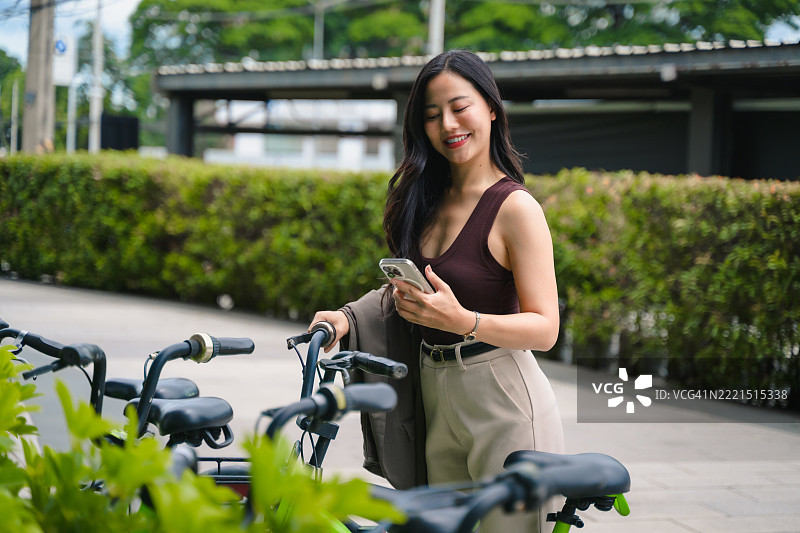 年轻的亚洲女商人在城市环境中使用共享单车时，正专注于她的智能手机。图片素材