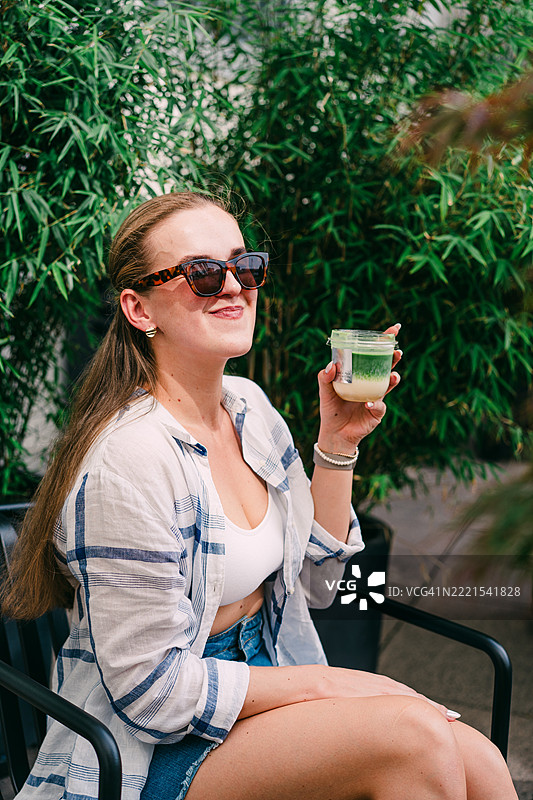 女性在宁静的花园环境中享受抹茶拿铁图片素材