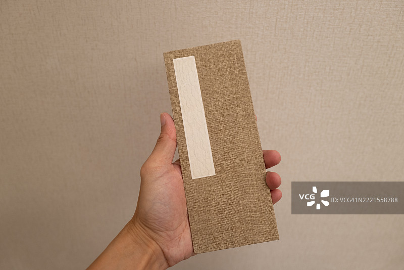 手握一个矩形物体，背景为中性色调图片素材
