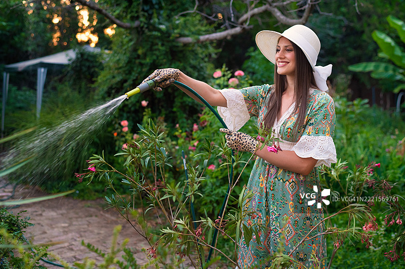 年轻女性在夏天的后院浇水植物图片素材