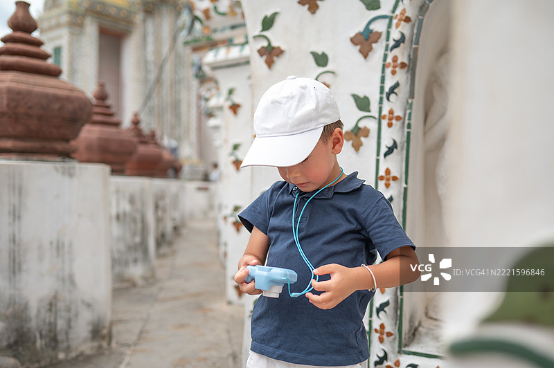 戴着白色帽子的男孩在泰国曼谷的阿伦寺庭院中用相机探索图片素材