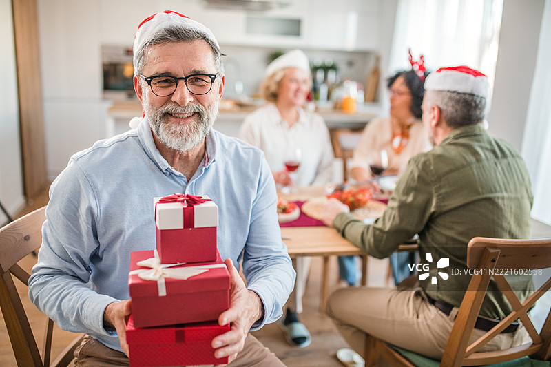 一位戴着眼镜的老年男子手里拿着装有圣诞礼物的盒子，正直视镜头。图片素材