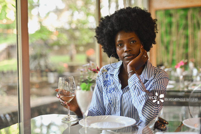 优雅的女性静静坐着，手持白葡萄酒，目光坚定地看向镜头。图片素材