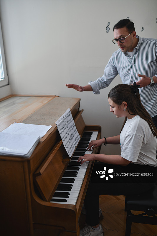 专注的男老师耐心地观看和倾听少女在钢琴练习时的演奏图片素材
