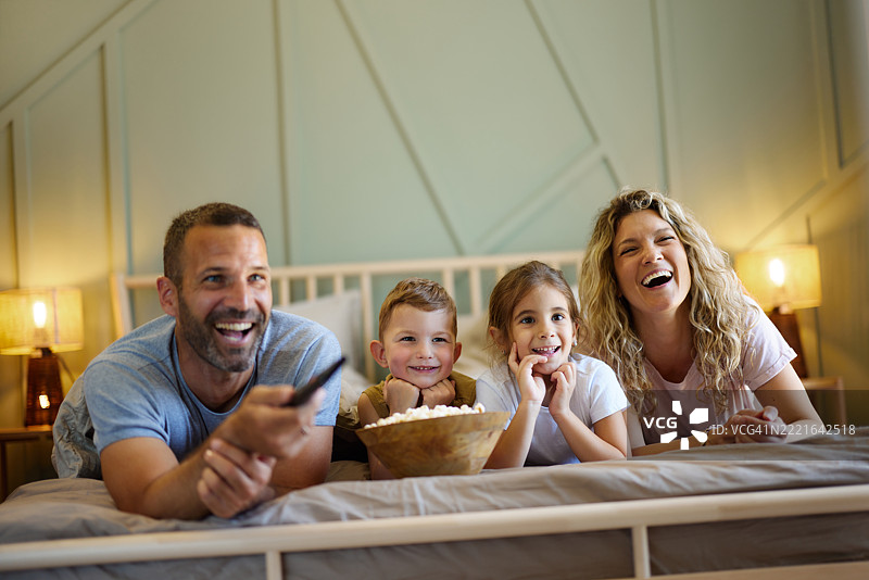 快乐的家庭在床上享受早晨时光，观看电视。图片素材