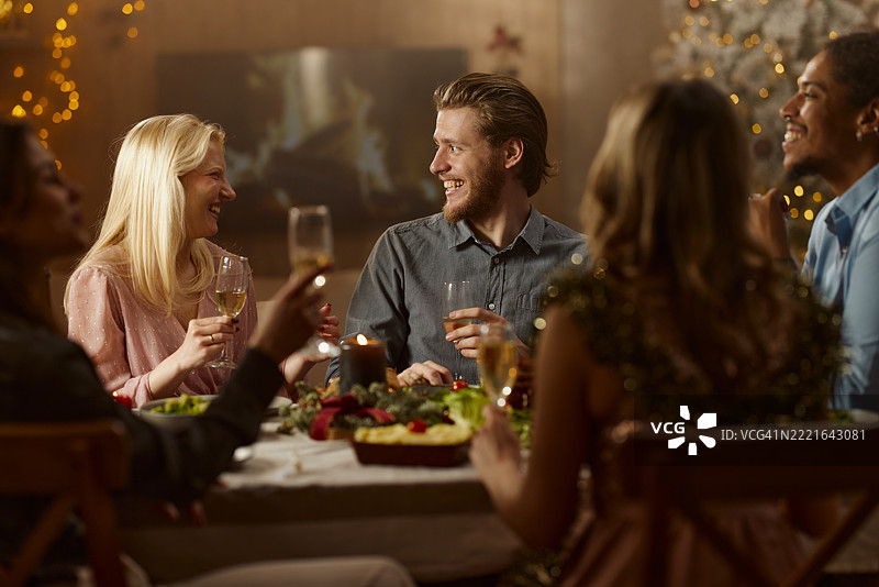 快乐的情侣在家与朋友们共度圣诞午餐，愉快地交谈。图片素材