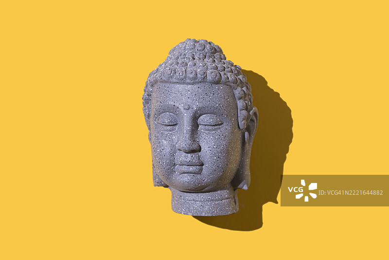 灰色石头佛像头部，背景为黄色。佛教，灵性，禅，神，信仰，和平，宁静，印度和泰国。图片素材