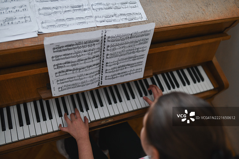 年轻钢琴家手部特写，正在练习乐谱旁的钢琴曲。图片素材