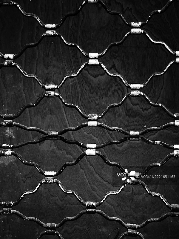 特写镜头：黑色木板前的，已破损并带有铜绿的卷式金属防护格栅。阳光。黑白。比利时布鲁塞尔。图片素材