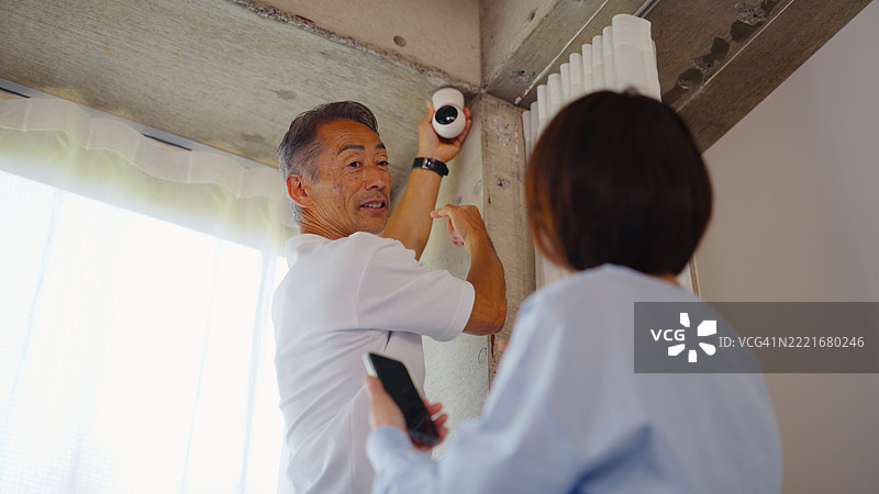 老年夫妇在客厅安装无线监控摄像头图片素材