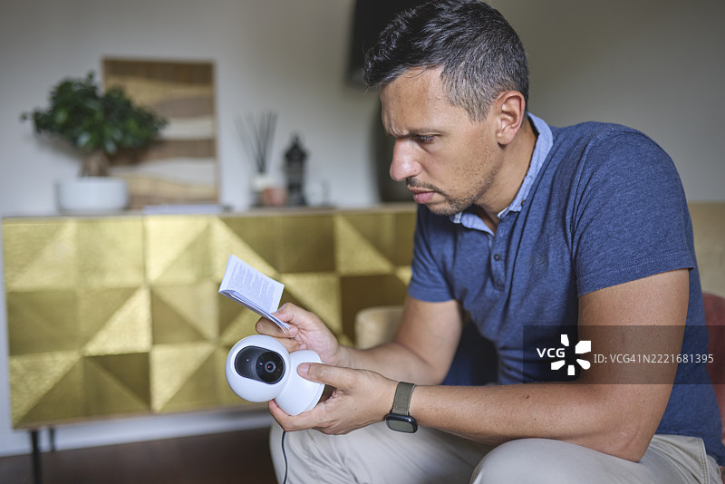 男子在桌子旁阅读智能监控摄像头的用户手册图片素材