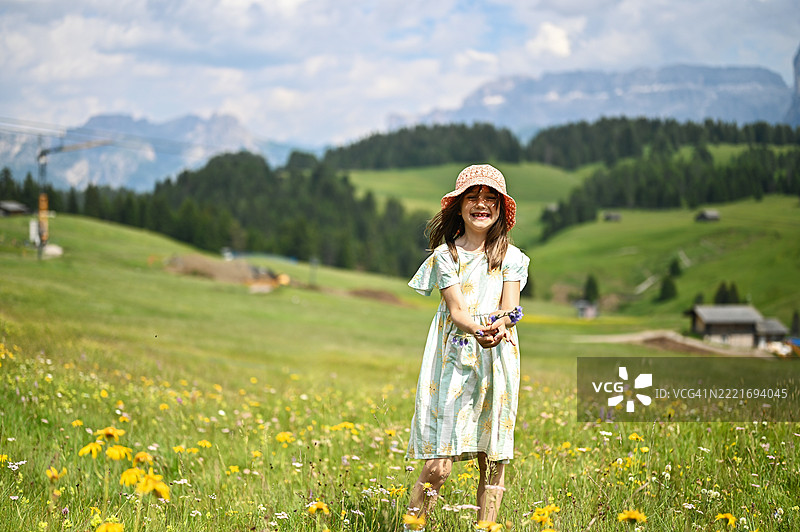 微笑的女孩在意大利多洛米蒂山的草地上捧着花朵图片素材