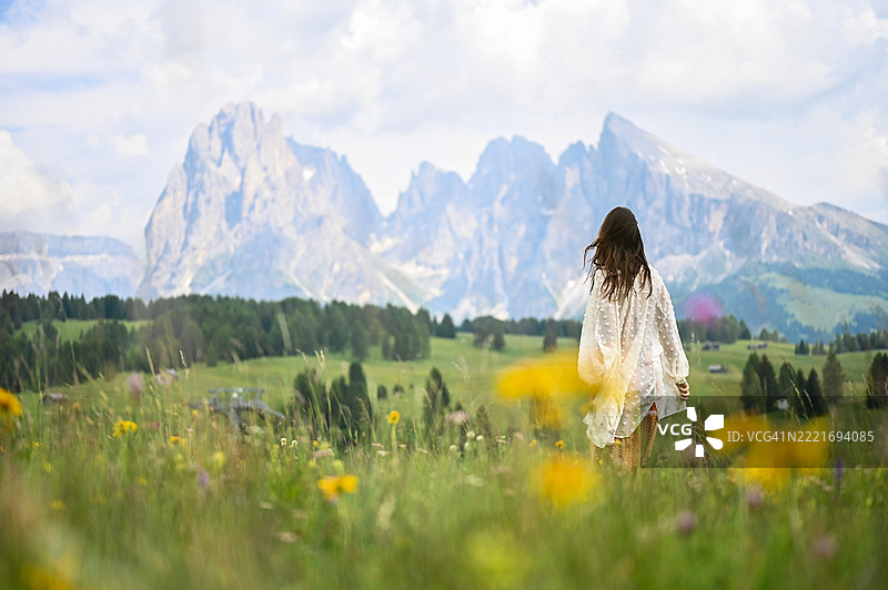 年轻女性在草地上漫步，背景是多洛米蒂山脉。图片素材
